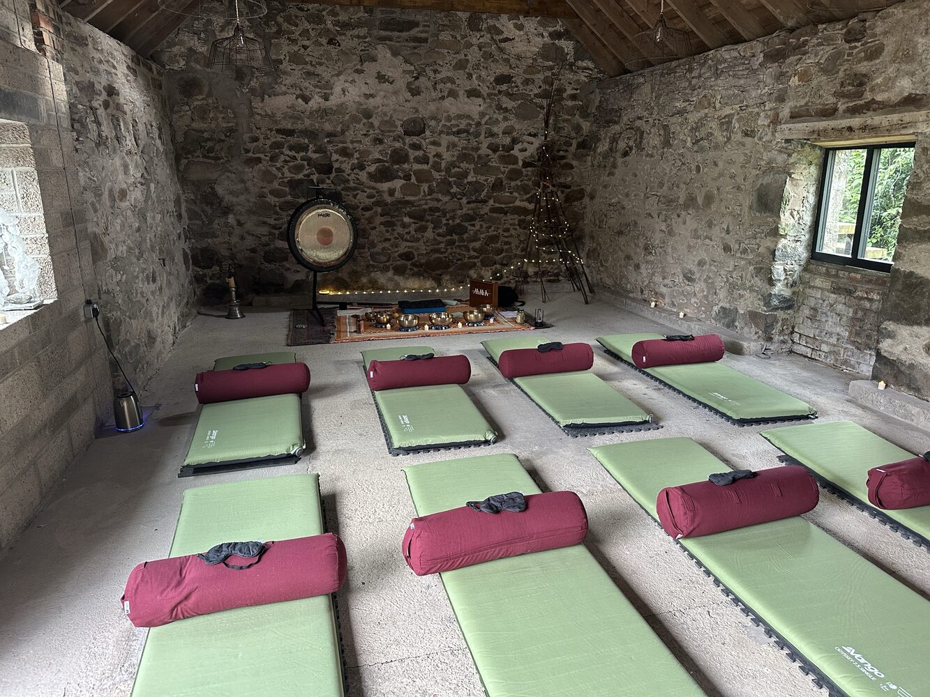 Sound bath mats, bolsters, bowls and gong arranged inside a rustic stone barn